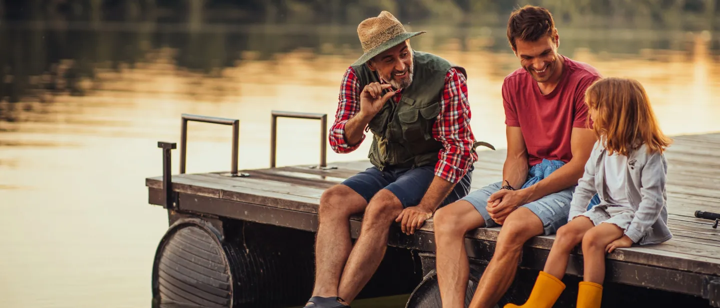 Two men sitting on a lake dock with a girl