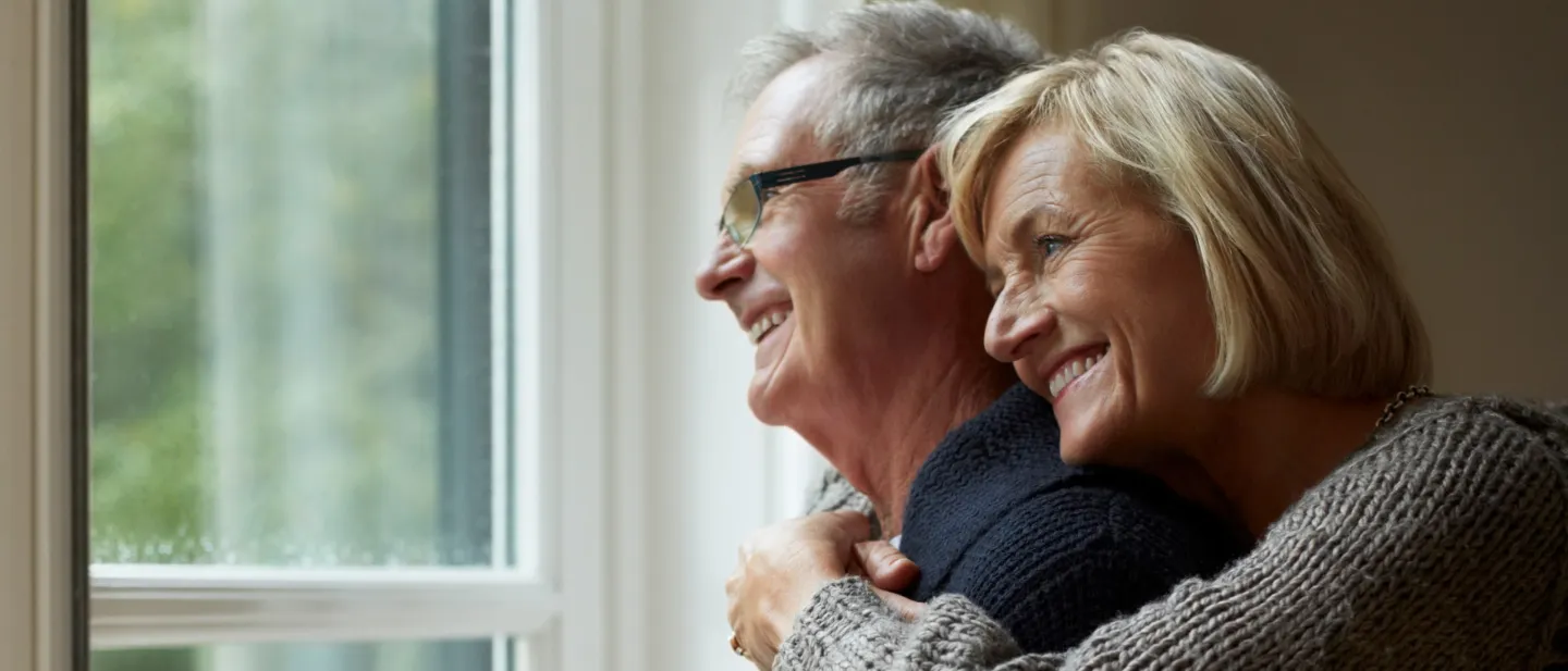 Older couple happily embracing and looking out a window