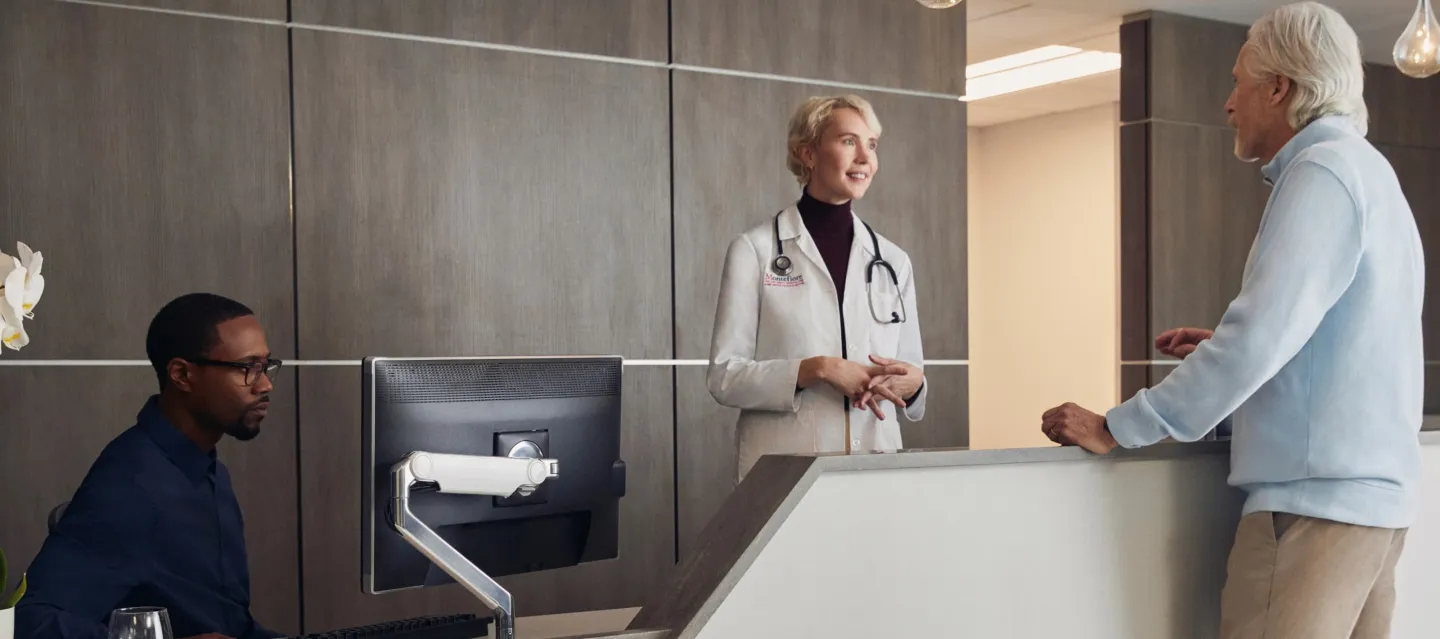 Hospital reception with two people taking and another looking at a computer screen.