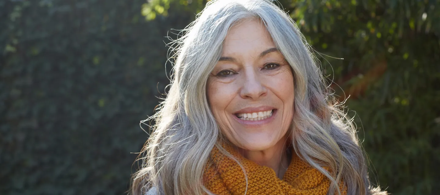 Woman with white hair smiling against a greenery background