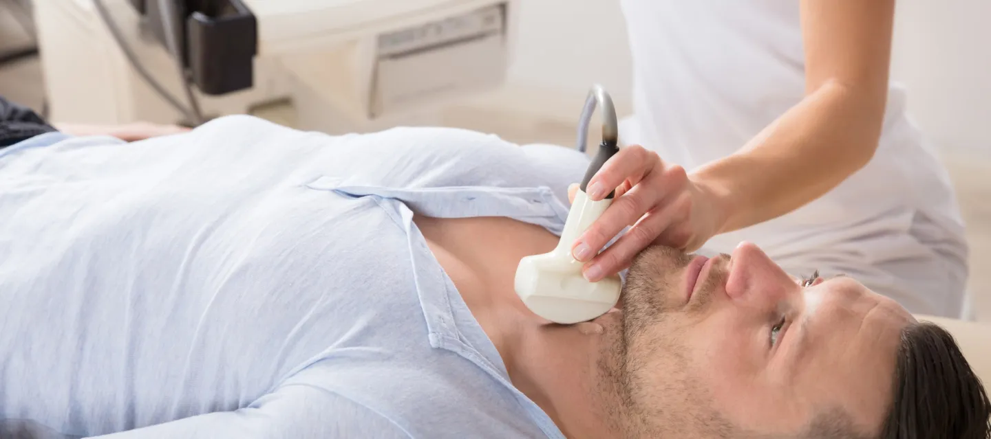 Man undergoing endocrinology examination with ultrasound machine by a technician