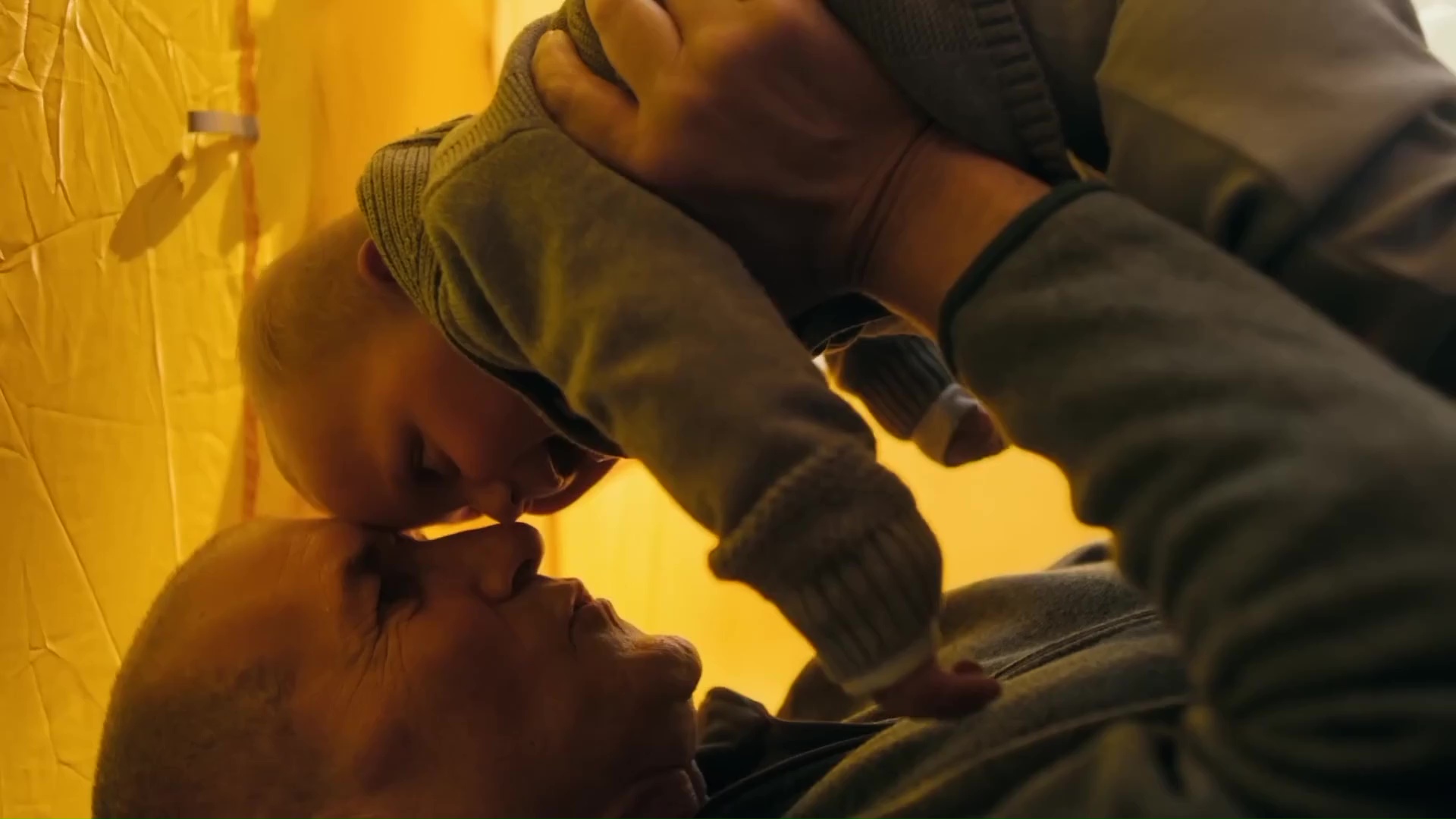 Father lying down while gently holding infant and touching noses. 