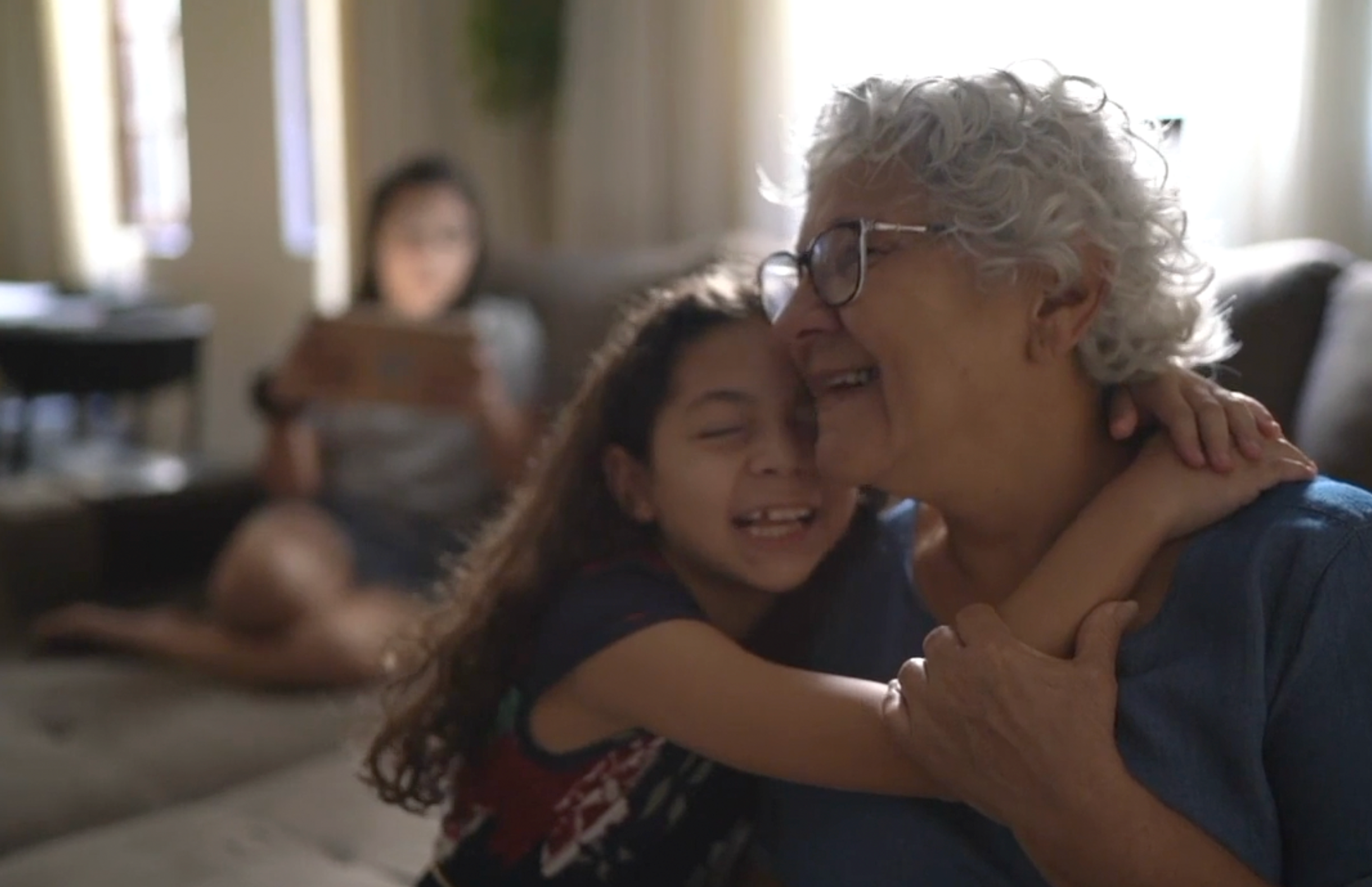 Child embracing grandmother seated with family members in background