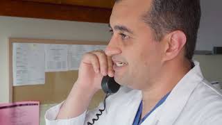 A doctor wearing scrubs and a white lab coat speaking on the telephone.