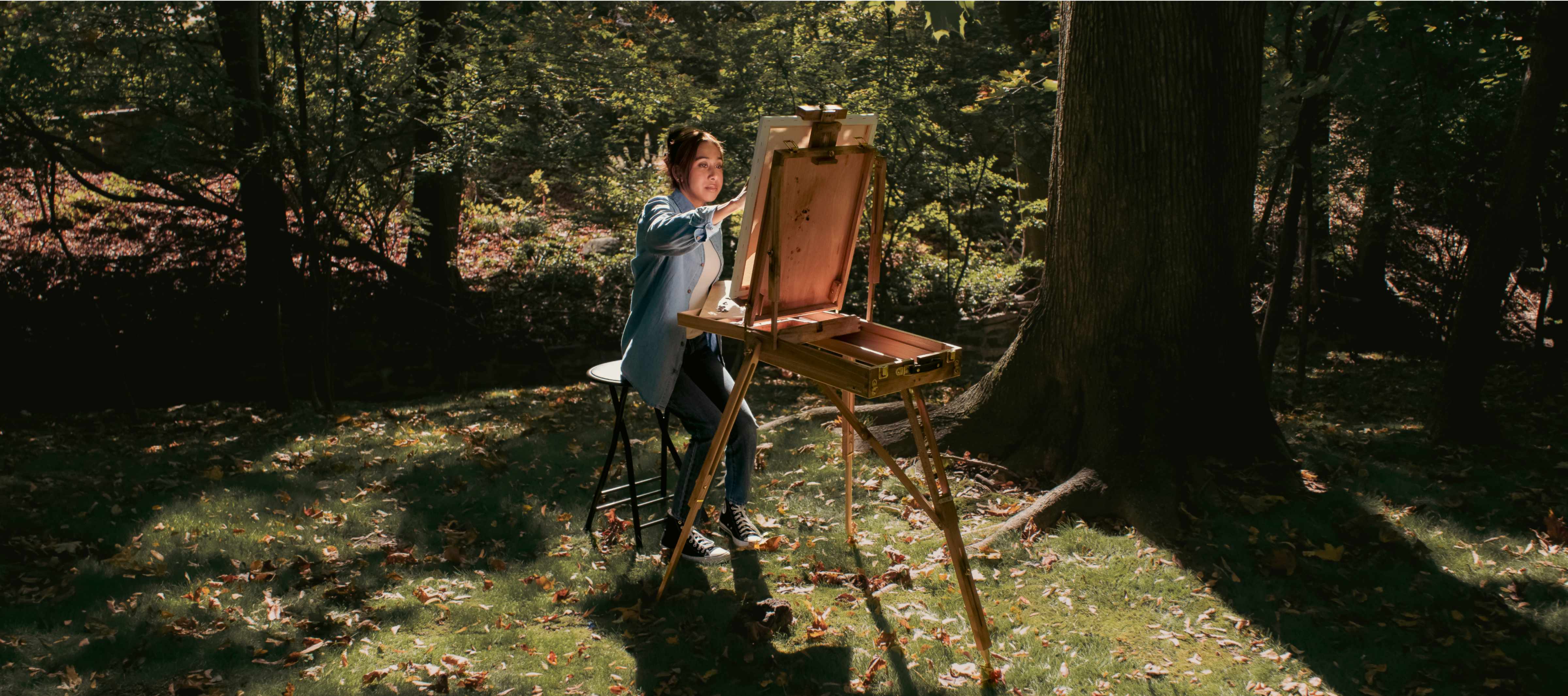 Pediatric kidney transplant recipient Alisha Khan in the woods, painting at an easel.