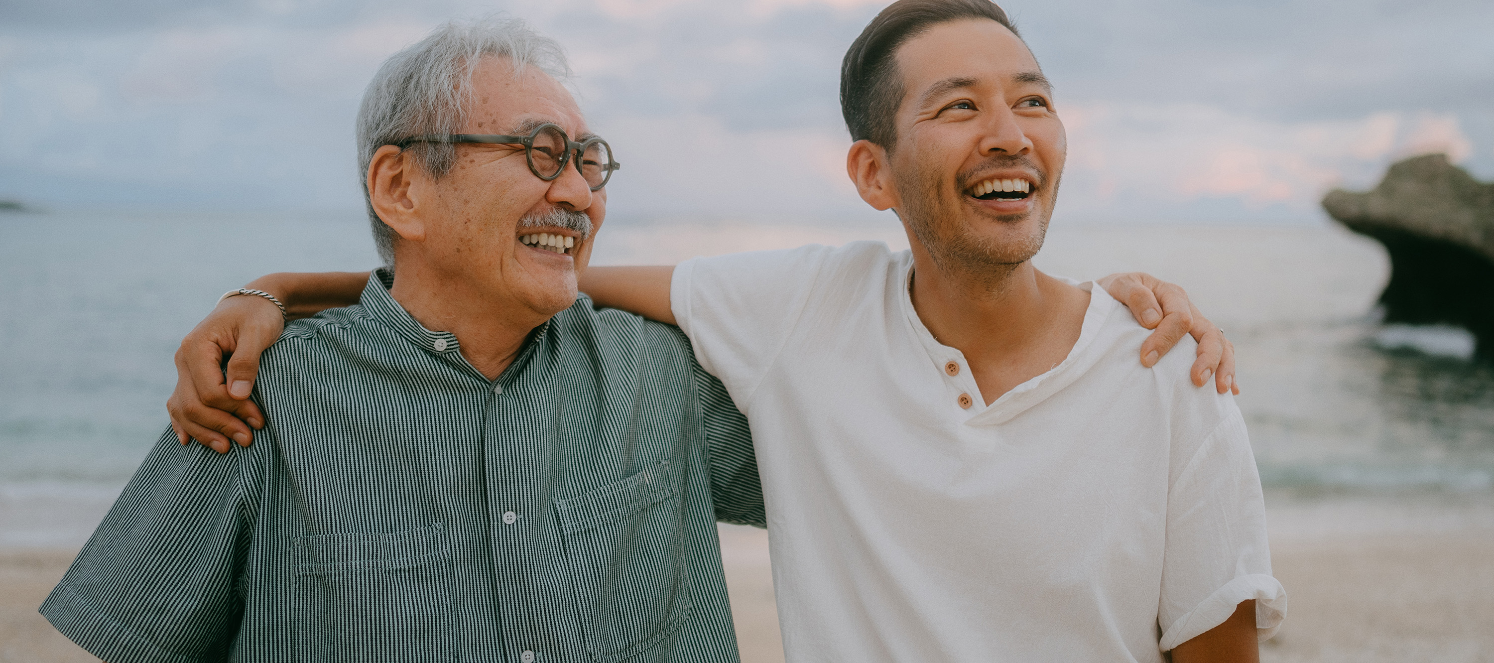 Smiling older man and younger man with arms around each other at the beach