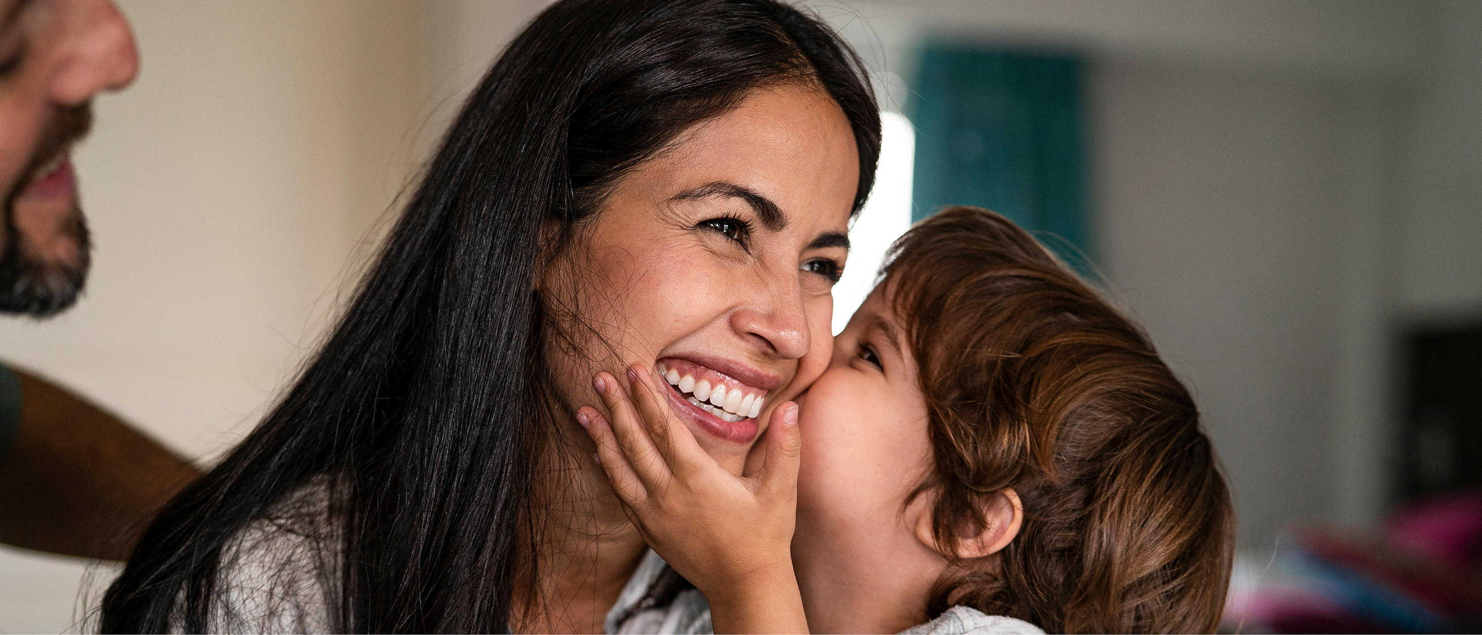 Smiling child kisses woman on the cheek as she laughs, close family moment