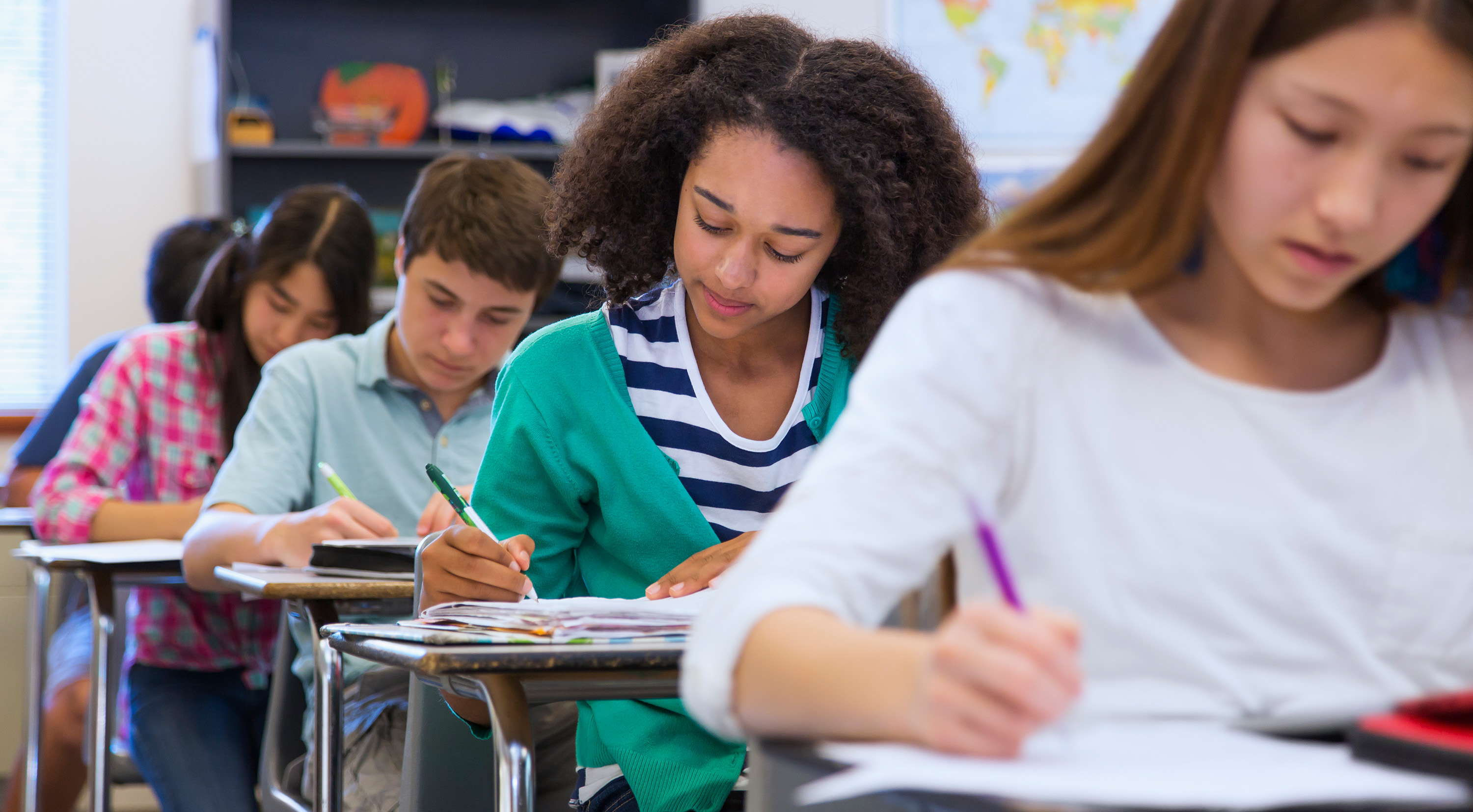Middle school students writing at desks in a classroom environment.