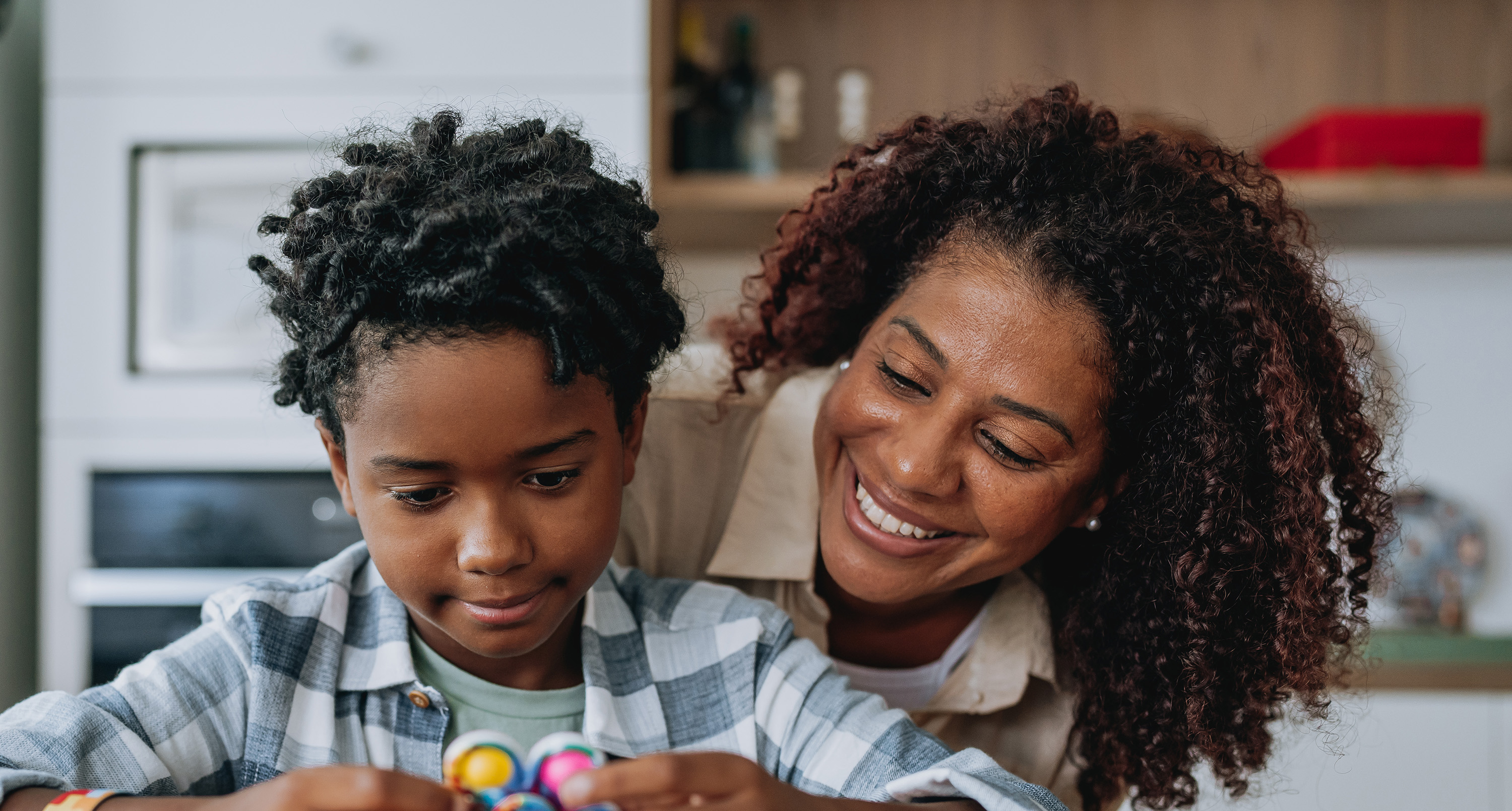 Mother and son smiling and playing with toys at a kitchen table.