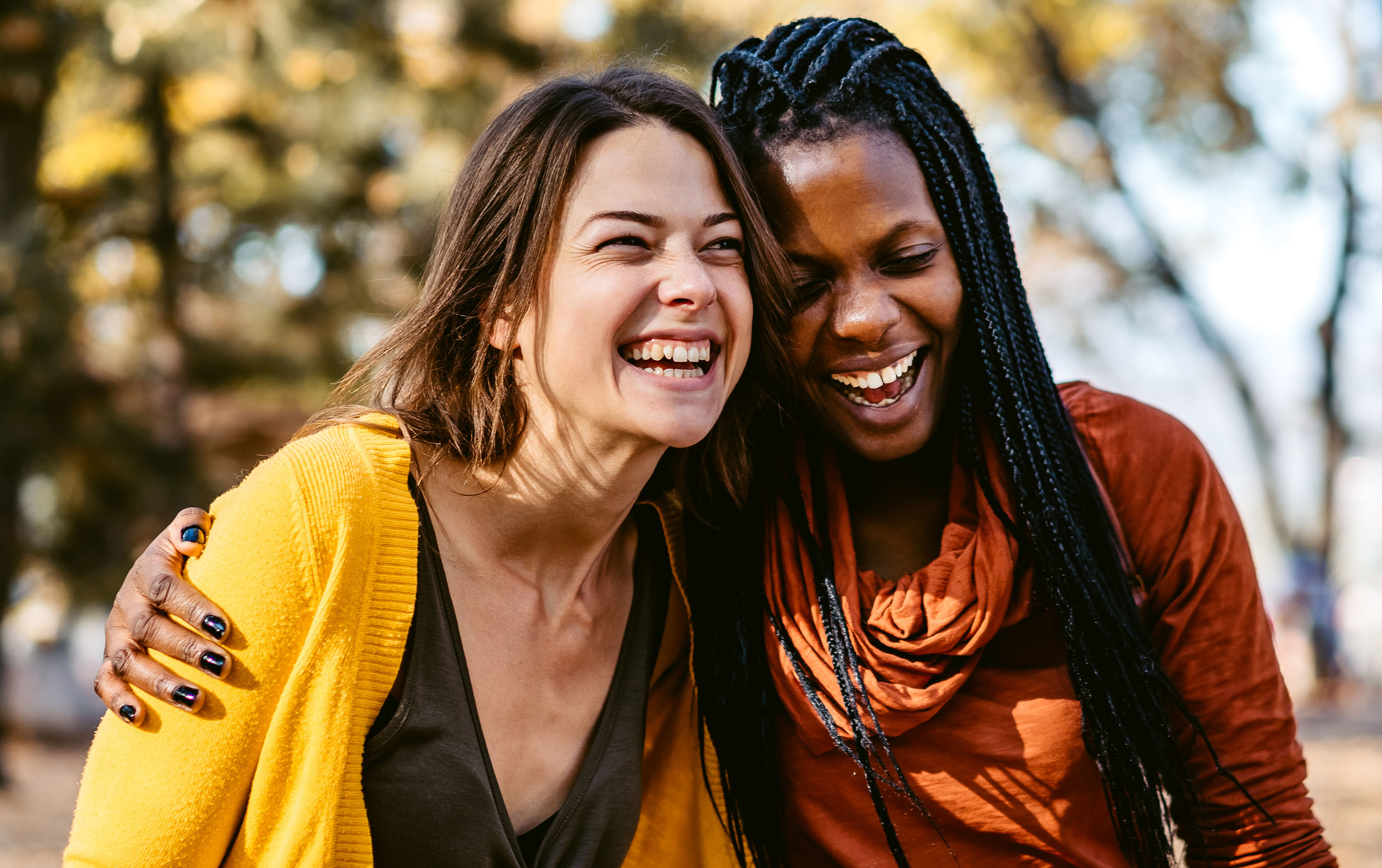 Two women laughing together in a park during autumn.