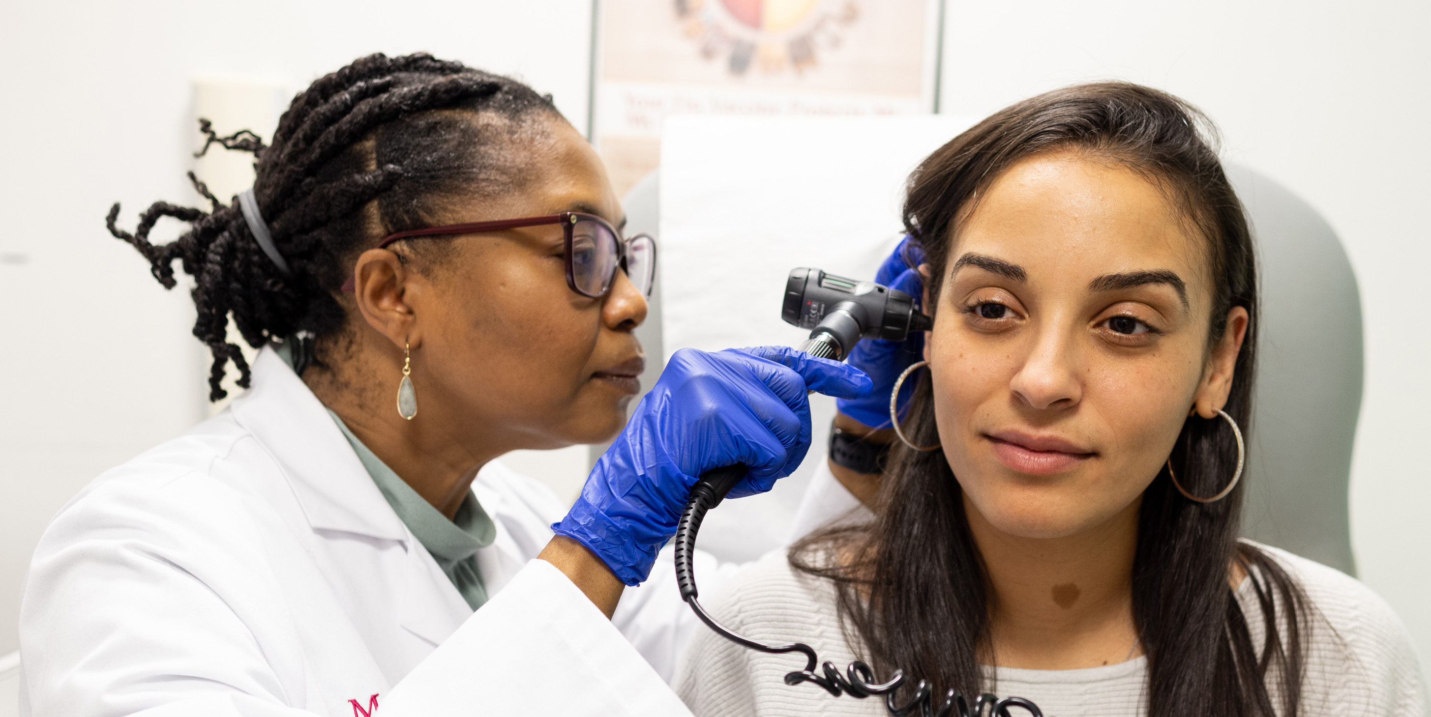 Female doctor examines a young woman’s ear using an otoscope in a medical office.