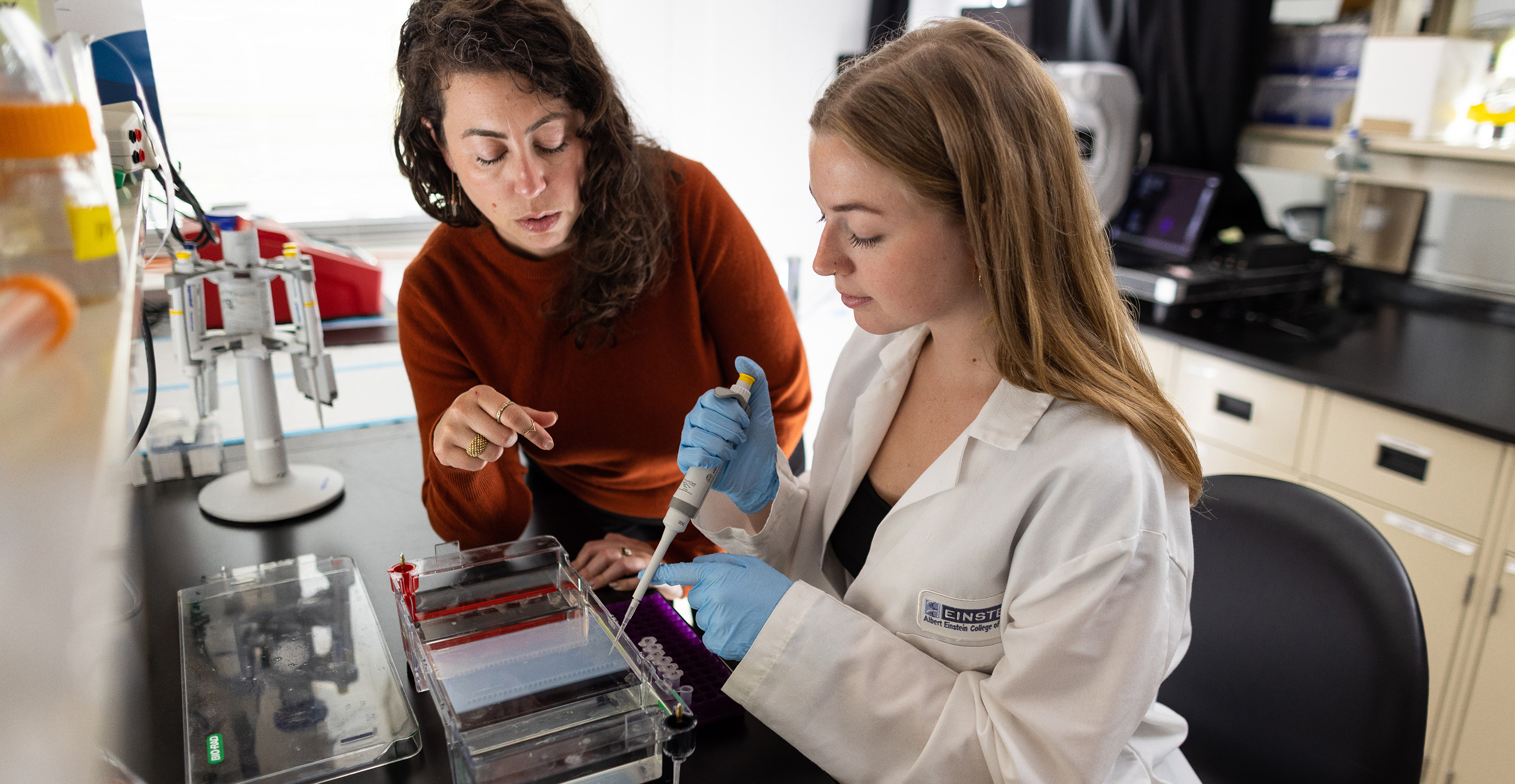  Two researchers working together in a laboratory, one using a pipette while the other provides guidance.