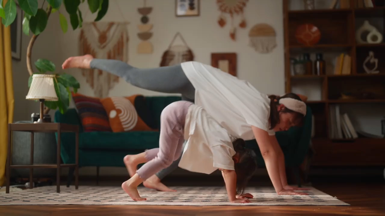 Mother and young daughter practicing yoga together in a cozy, bohemian-style living room.