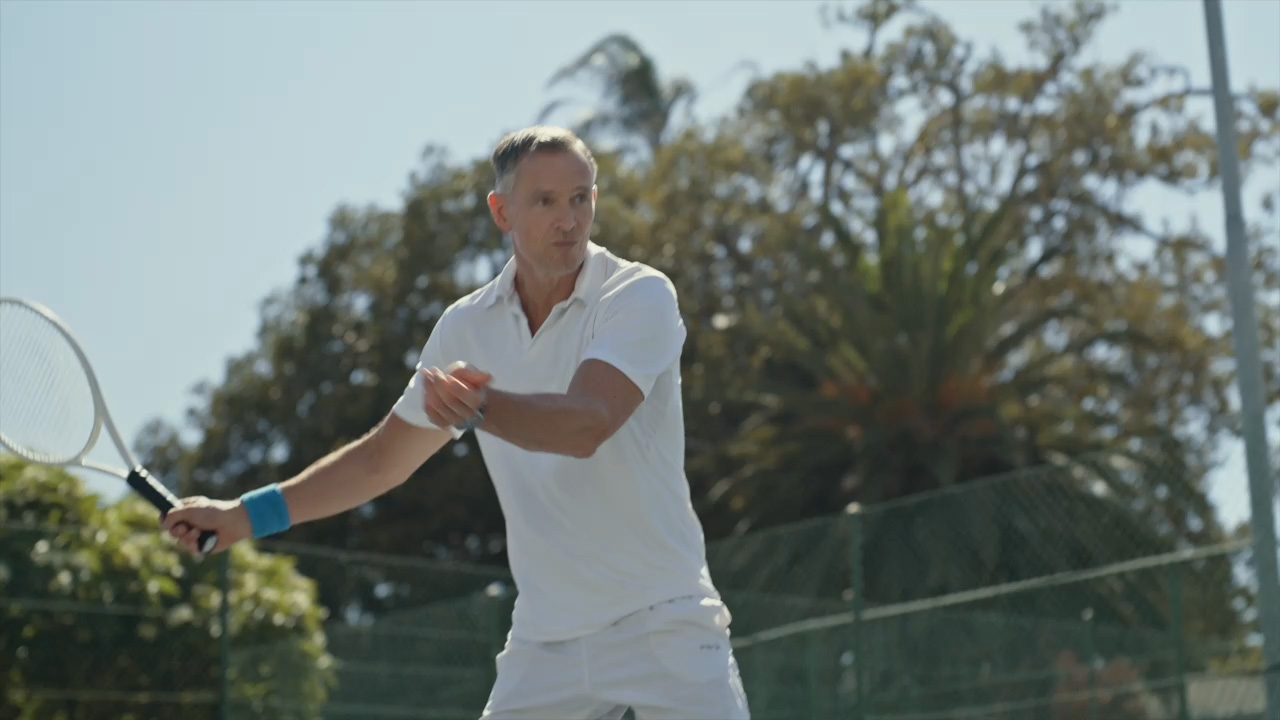 Man in white tennis outfit swinging a racket on an outdoor court.
