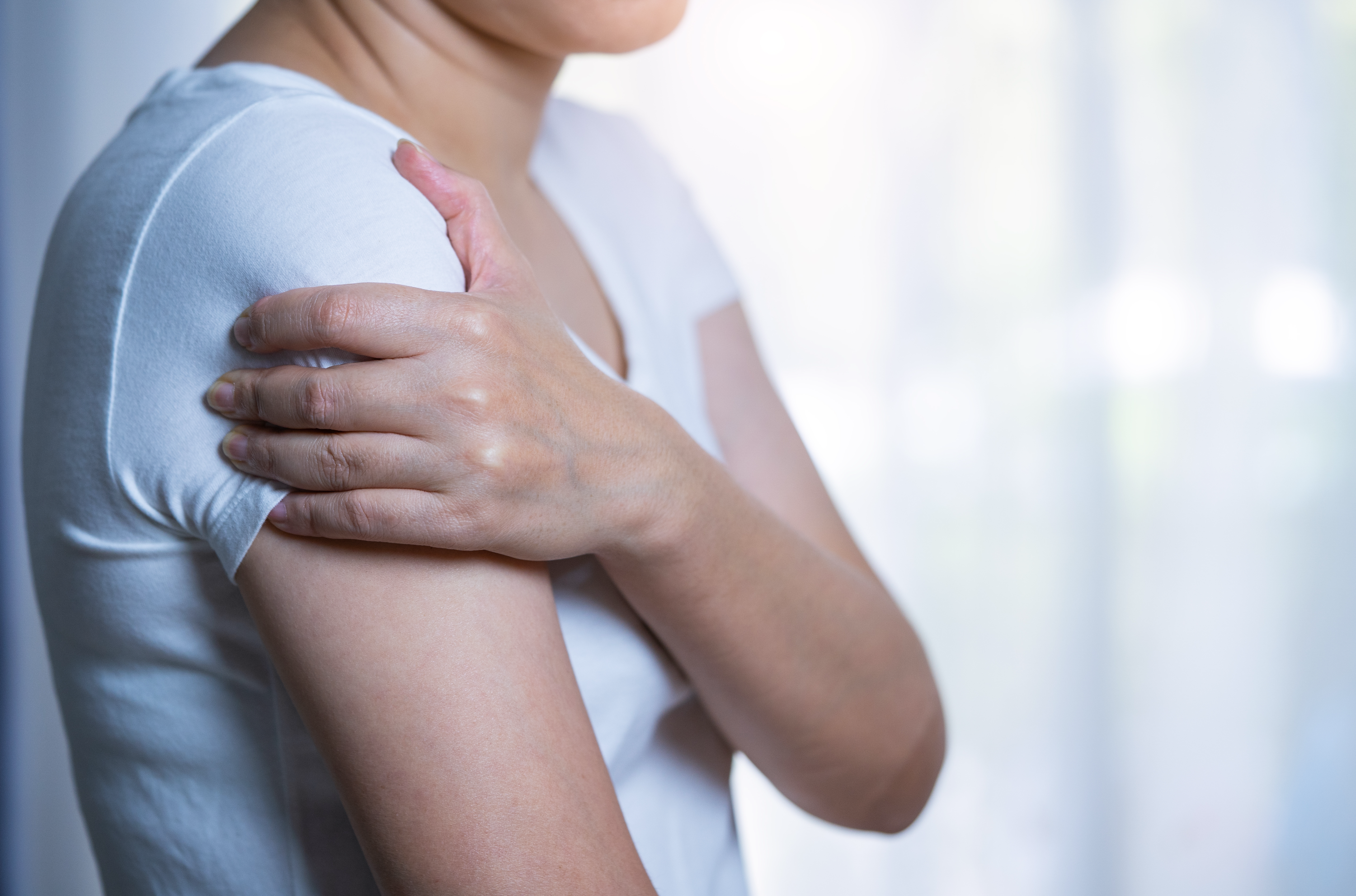 Woman wearing a white T-shirt and holding her shoulder with her left hand
