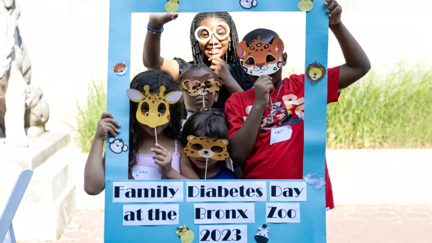 Kids posing with animal masks inside handmade paper frame with the words "Family Diabetes Day at the Bronx Zoo 2023"