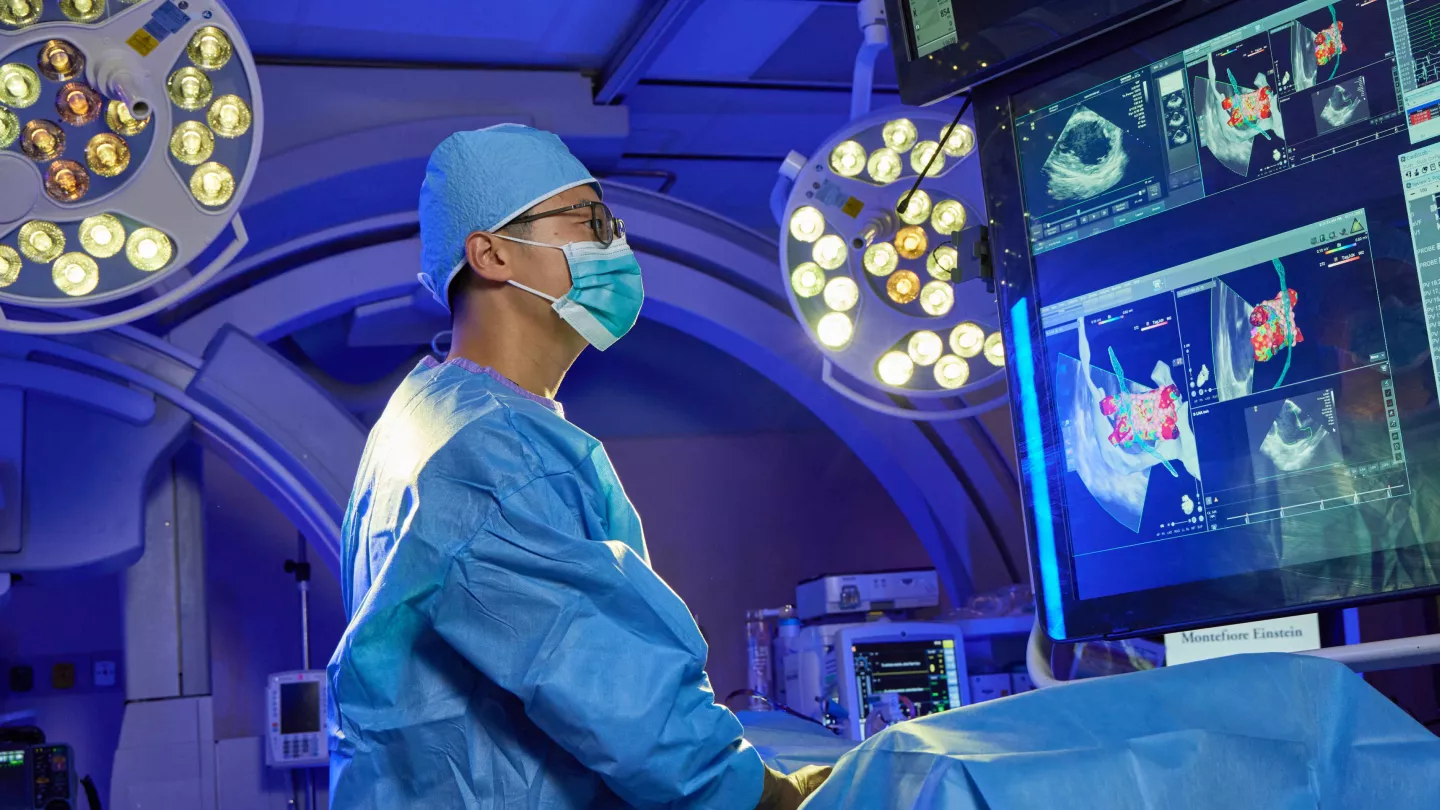 Montefiore Einstein doctor in operating theater, wearing scrubs and surgical mask and viewing imagery on large screens.
