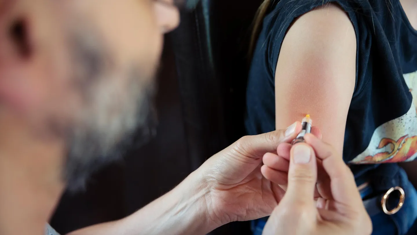 Over the shoulder view of Doctor giving HPV vaccination to teenager in a home environment