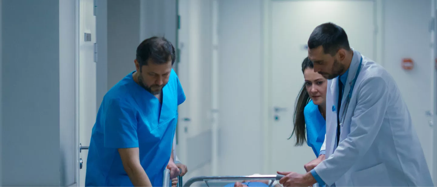 Emergency clinicians and staff moving down a hallway while attending to patient lying down on a gurney