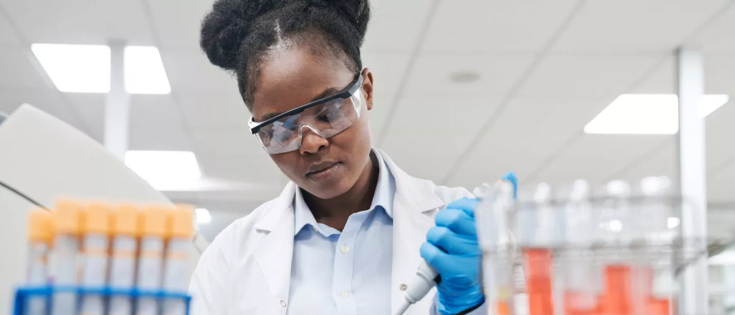Female scientist wearing safety eyewear in brightly lit laboratory holding pipette filling vials