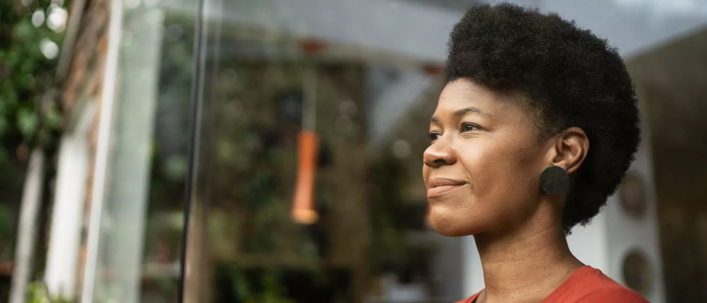 A woman with short curly hair smiling while looking through a window