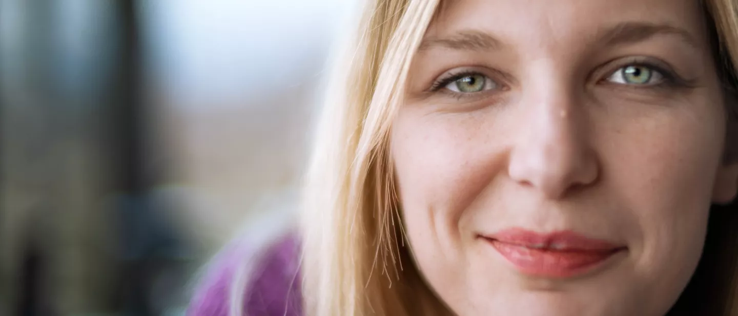 Close-up of a smiling woman with blonde hair and green eyes looking at the camera