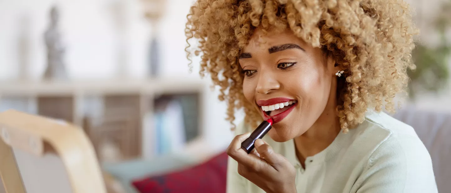 Smiling woman applying red lipstick while looking into a mirror at home