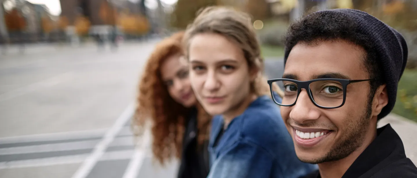 Three young people sitting on a bench, smiling and looking at the camera.