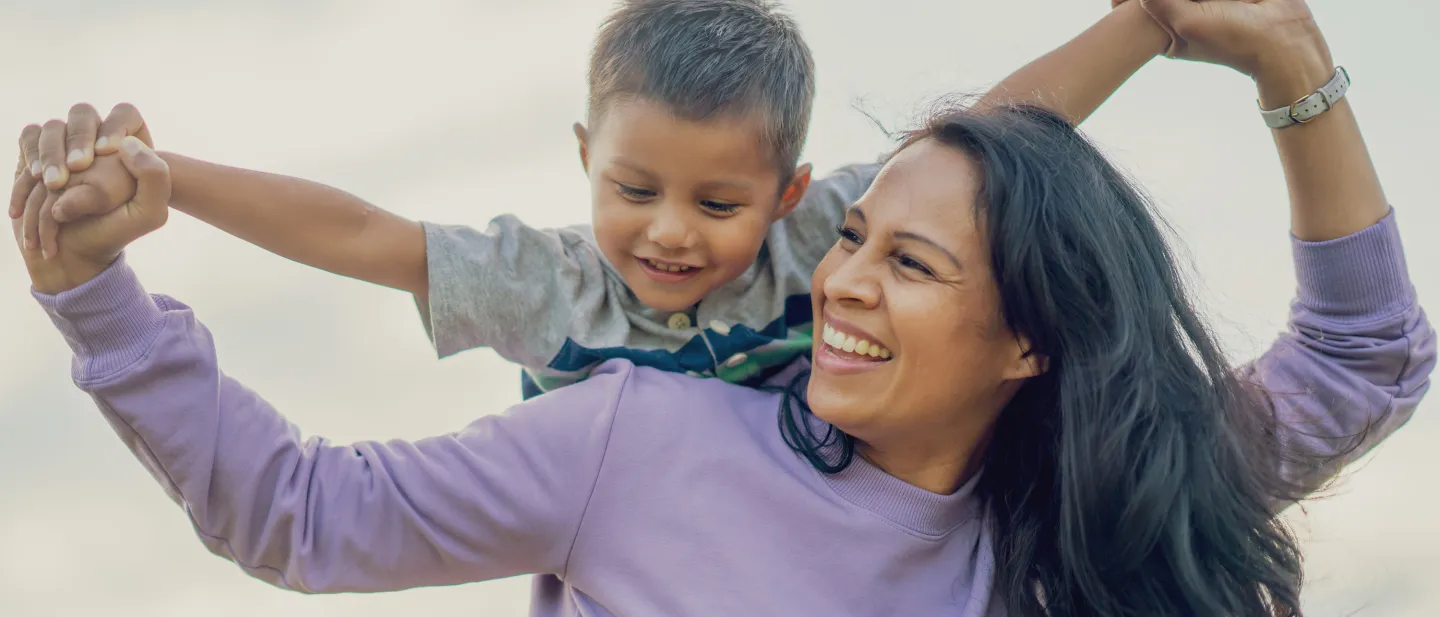 Happy mother giving her young son a piggyback ride while holding hands outside