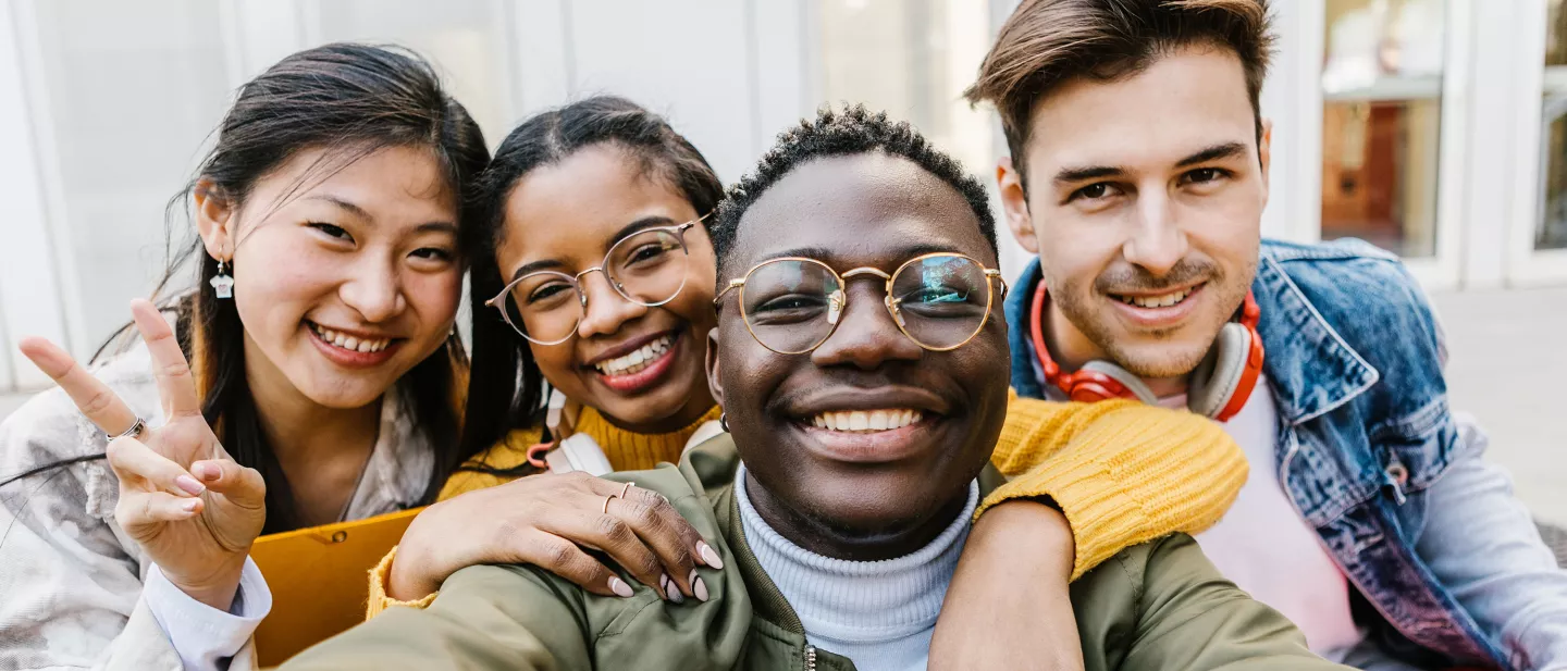 Group of four young adults smiling and taking a selfie outdoors