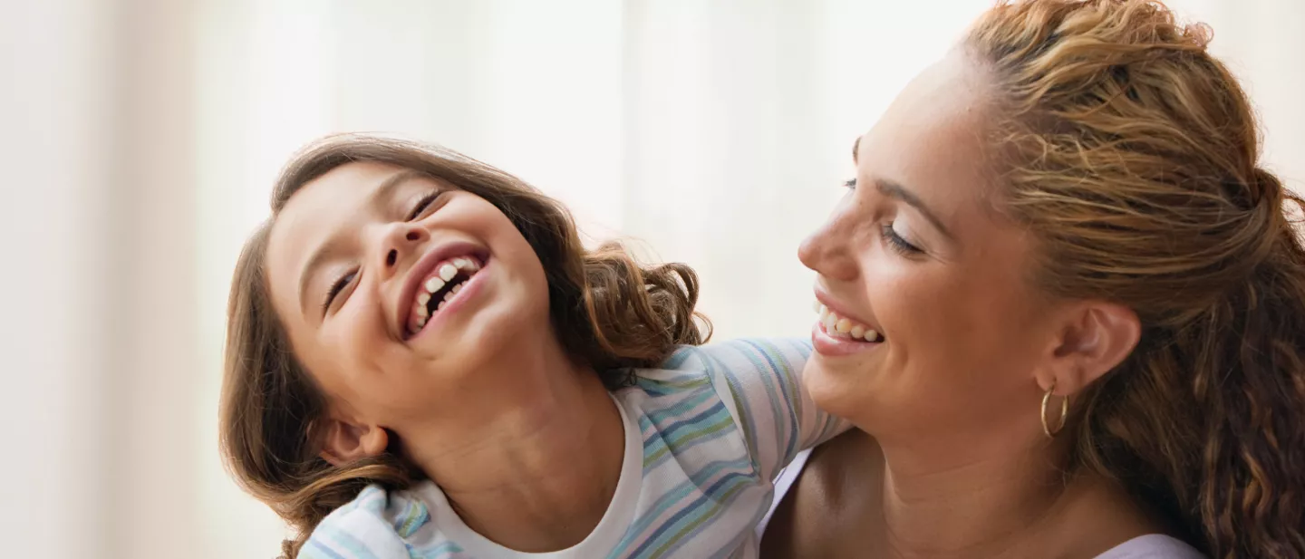 Mother and daughter laughing together indoors, sharing a joyful moment