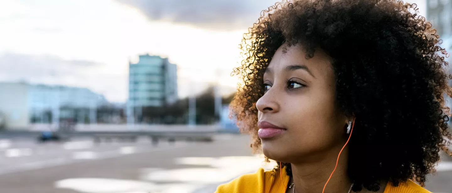 Young woman with curly hair wearing earbuds gazing into the distance