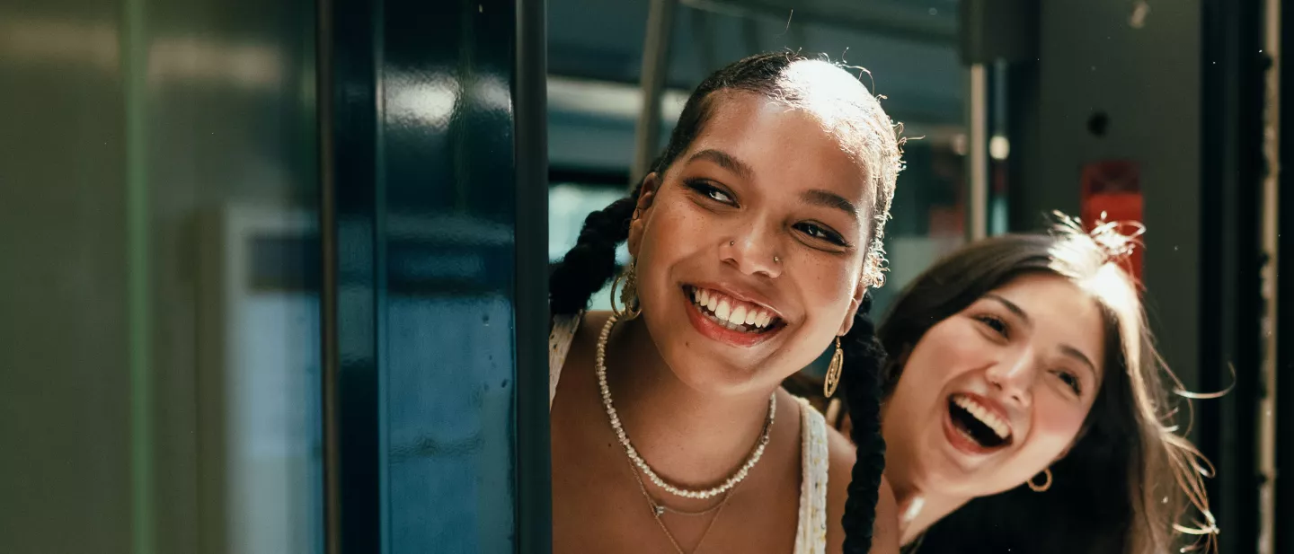 Two young women laughing and leaning out of a bus or train door, enjoying a joyful moment together
