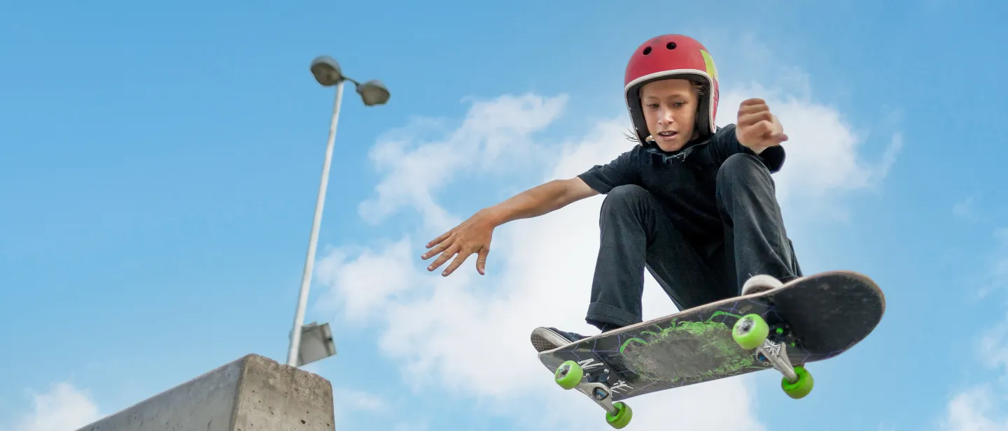 Teen skateboarder wearing helmet doing a trick mid-air at a skatepark