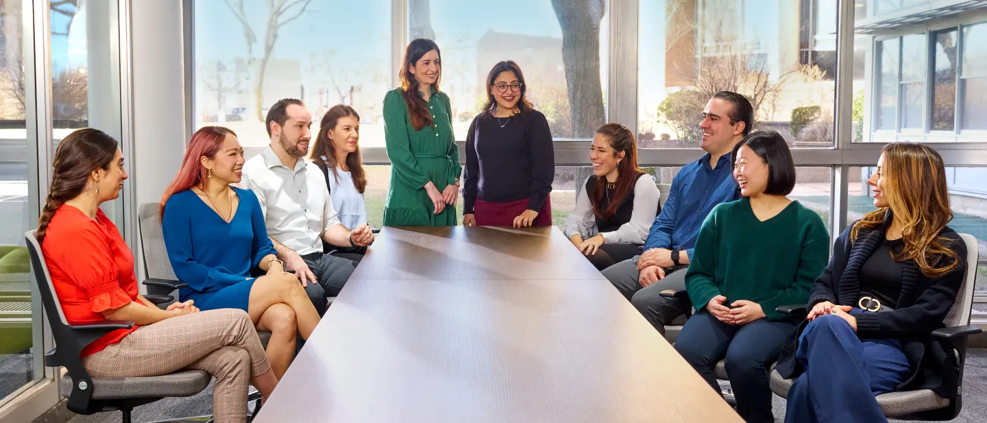 Group of colleagues smiling and talking around a large table in a bright conference room