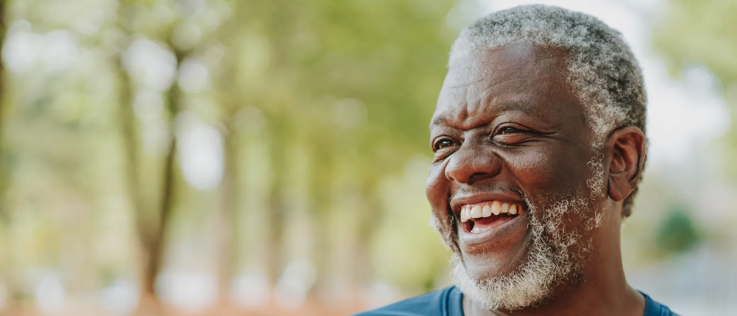 Older man laughing joyfully during a walk through a tree-lined park.