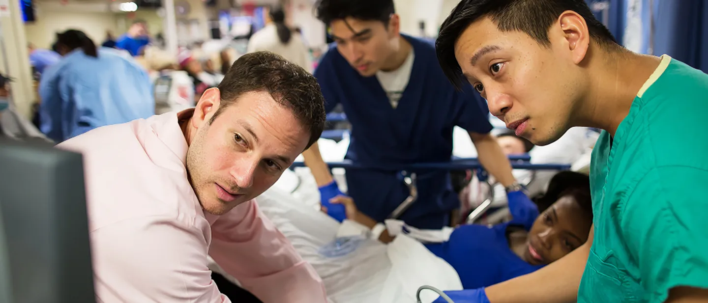 Physicians and residents crowd around a patient in a busy emergency department, intently focused on an ultrasound screen.