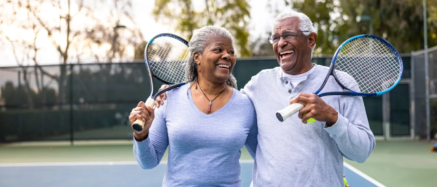 Man and woman holding tennis rackets laughing.