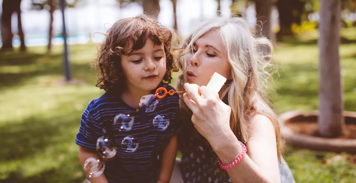 A grandmother and grandson blowing bubbles in a garden during the summer.