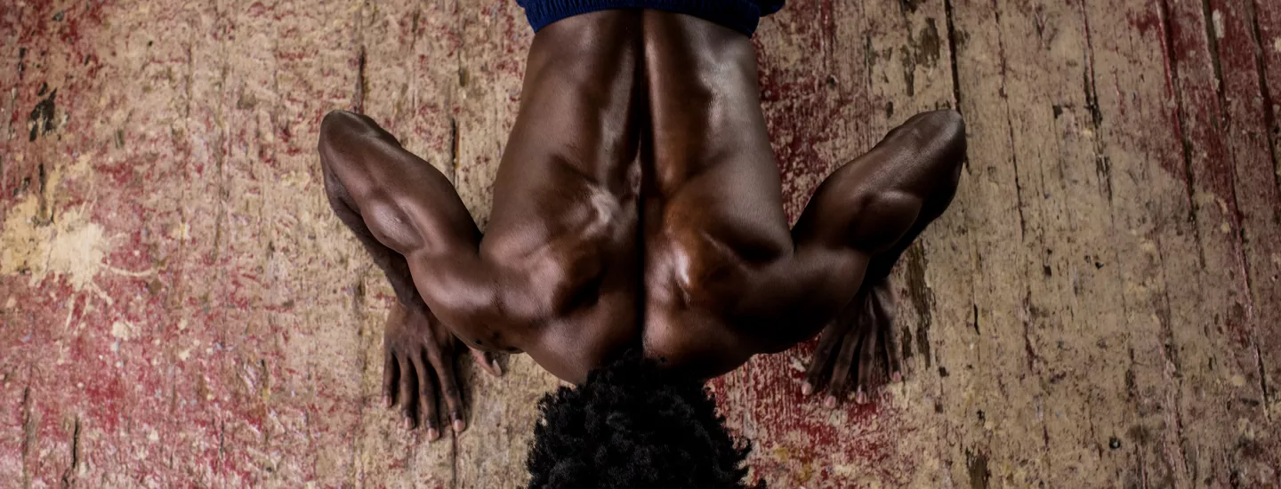A man doing push-ups on a wooden floor; only the back of his head, his back and part of his workout pants are depicted.