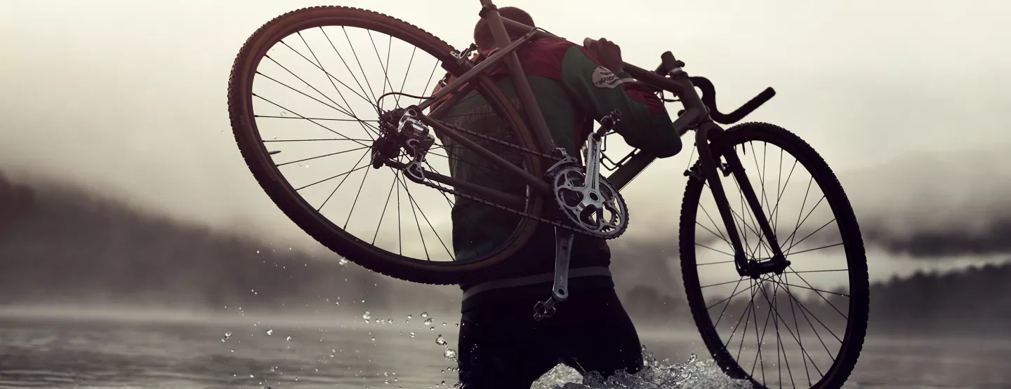 A man wading through water with a bike on his right shoulder