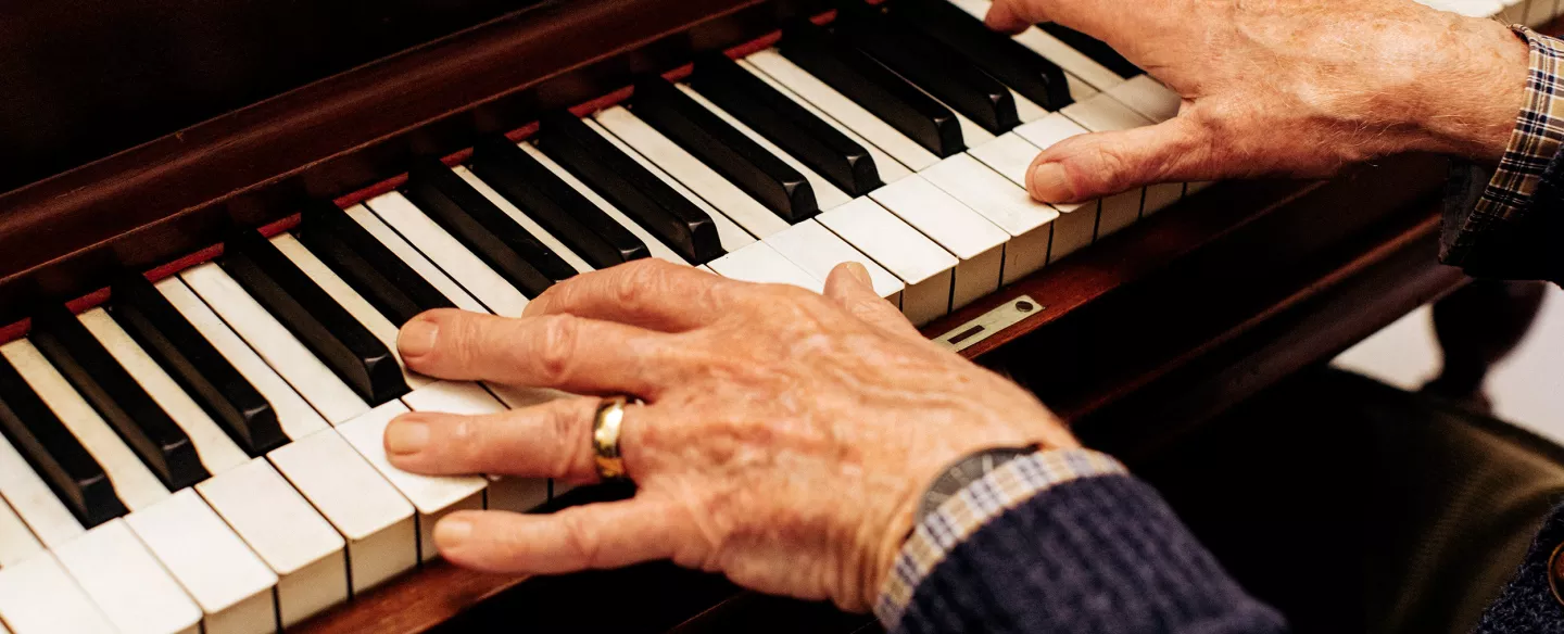 The hands of an older man playing a piano.