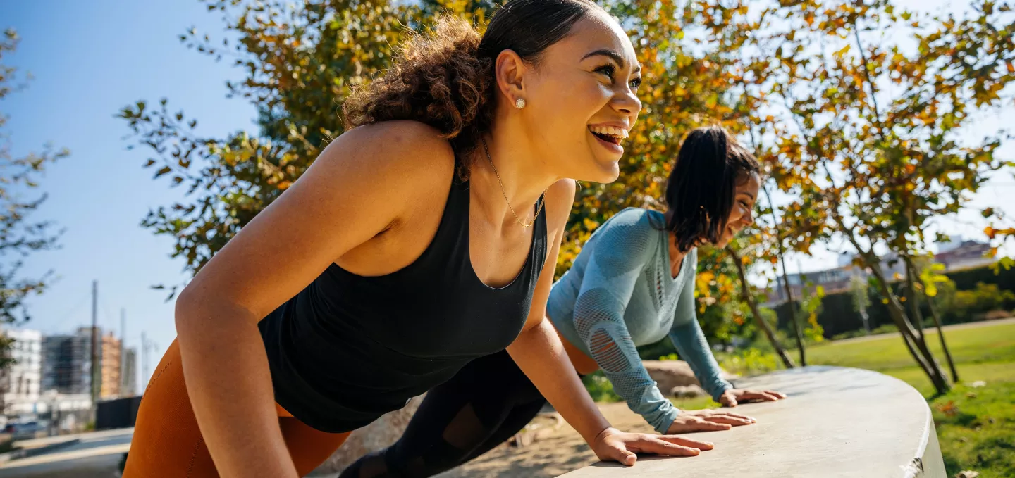 Cheerful women doing push-ups on retaining wall at park
