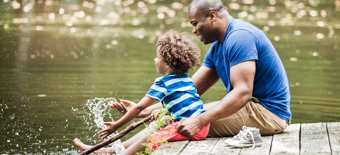 A father and his young son splashing water while sitting in a dock