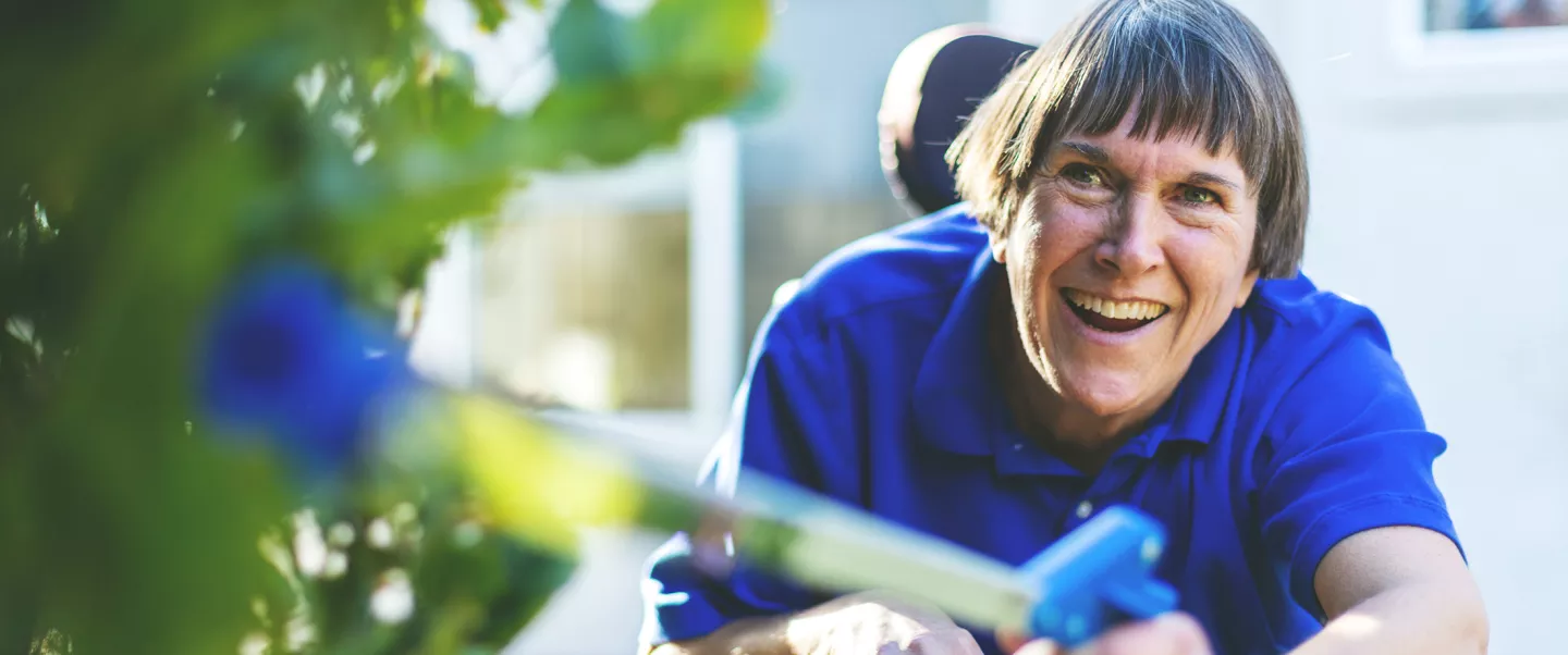An older woman in a wheelchair sitting in a garden smiling
