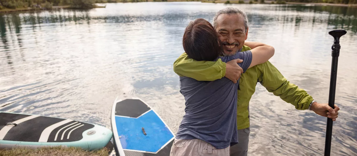 A man and woman hugging by a lake.