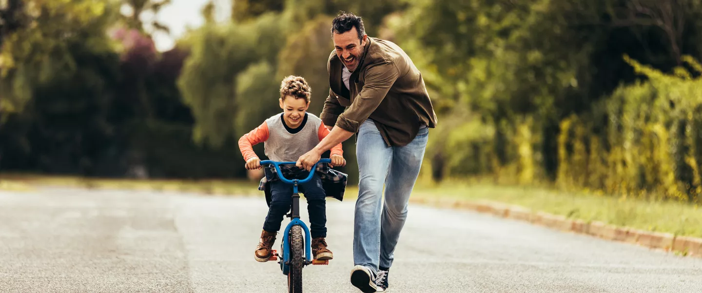 A happy kid having fun learning to ride a bicycle with his father.