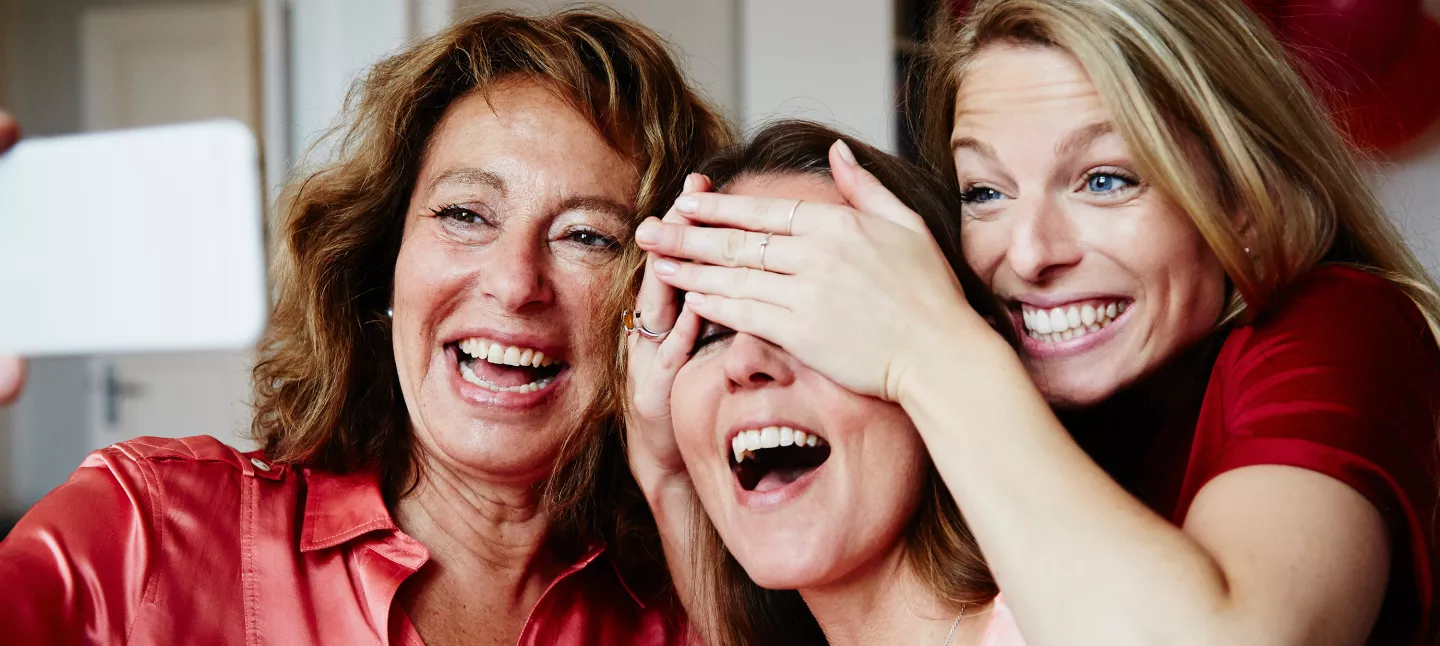 A mother with her adult daughters laughing while taking a selfie photo
