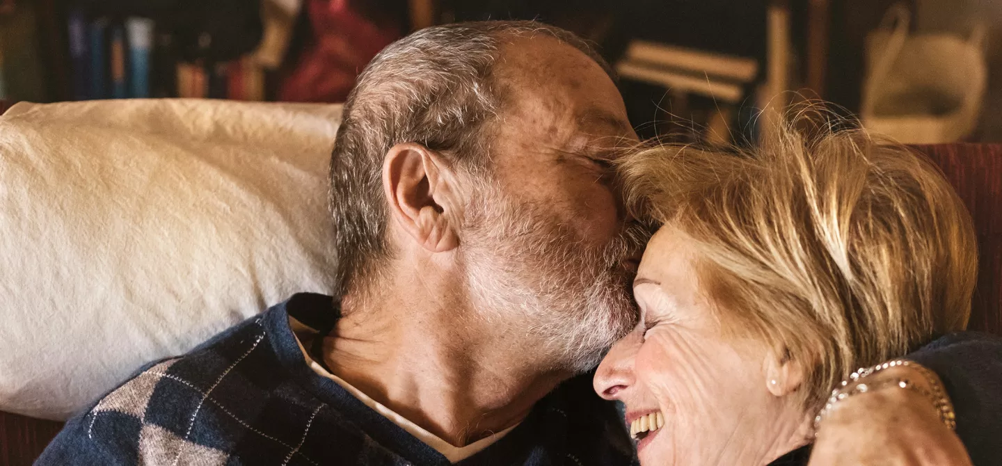 Happy and playful senior couple together at home. Man kisses woman on the forehead.