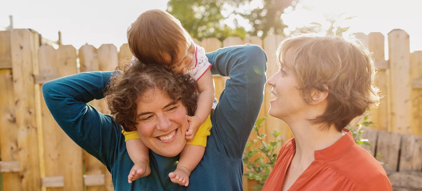A woman holding a baby in front of a fence.